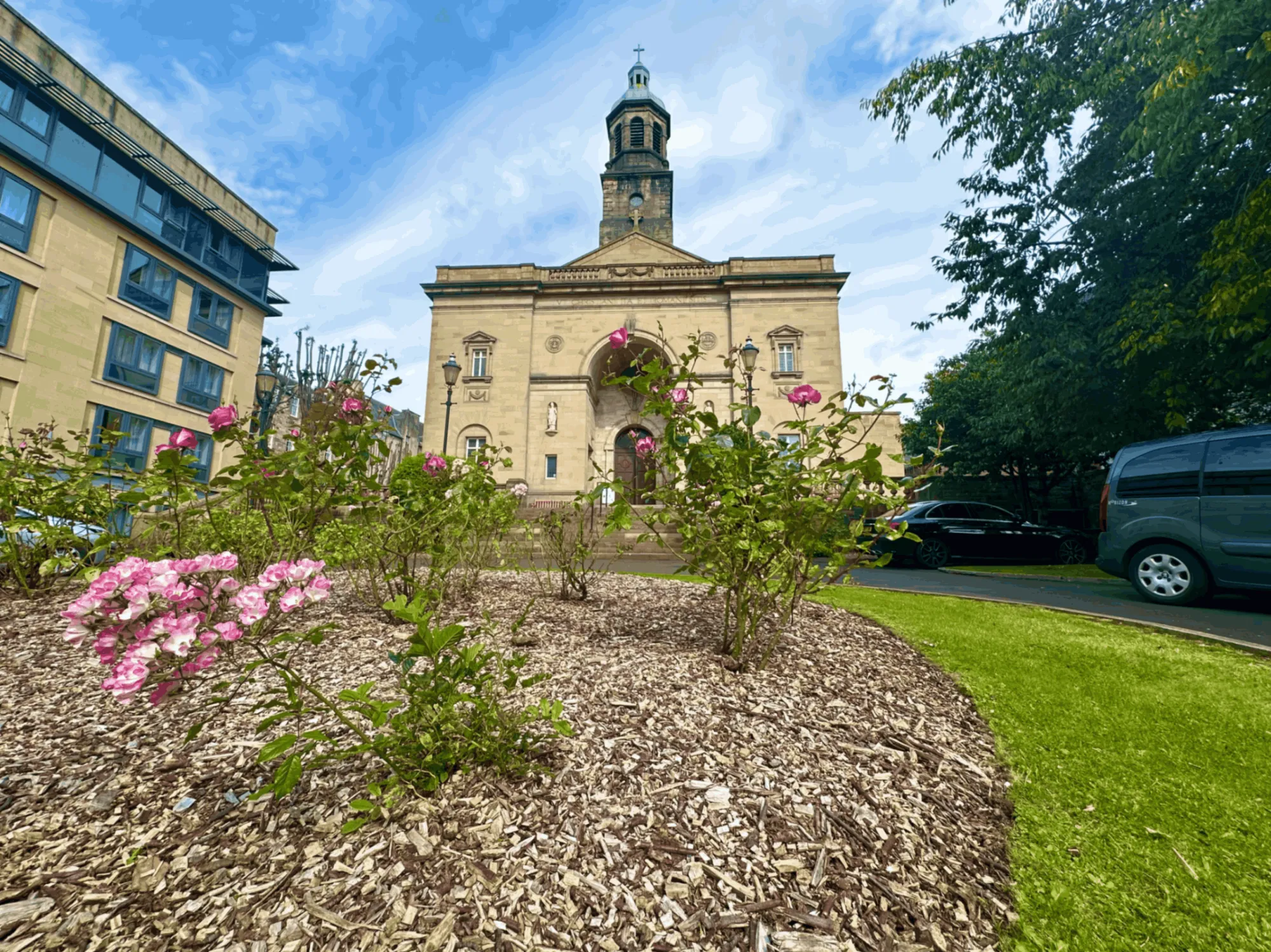 Well-maintained rose beds with fresh wood chip mulch located in the grounds of a historic stone church building.