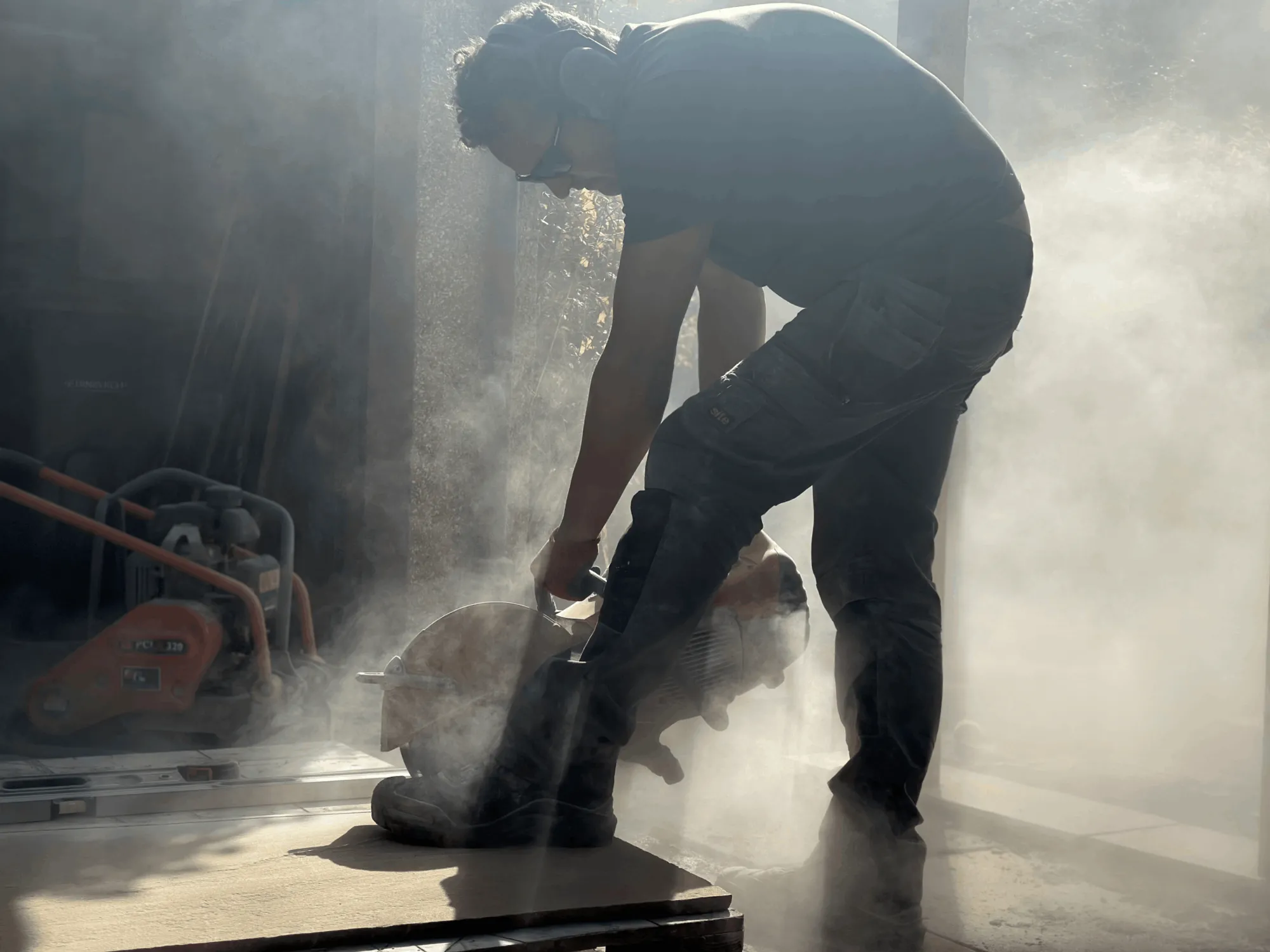 A professional landscaper cutting stone paving slabs with a circular saw, creating dust during construction.