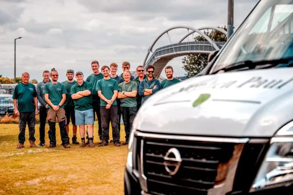 The Stephen Paul Gardens team standing together in the distance, framed by the branded bonnet of a company van.