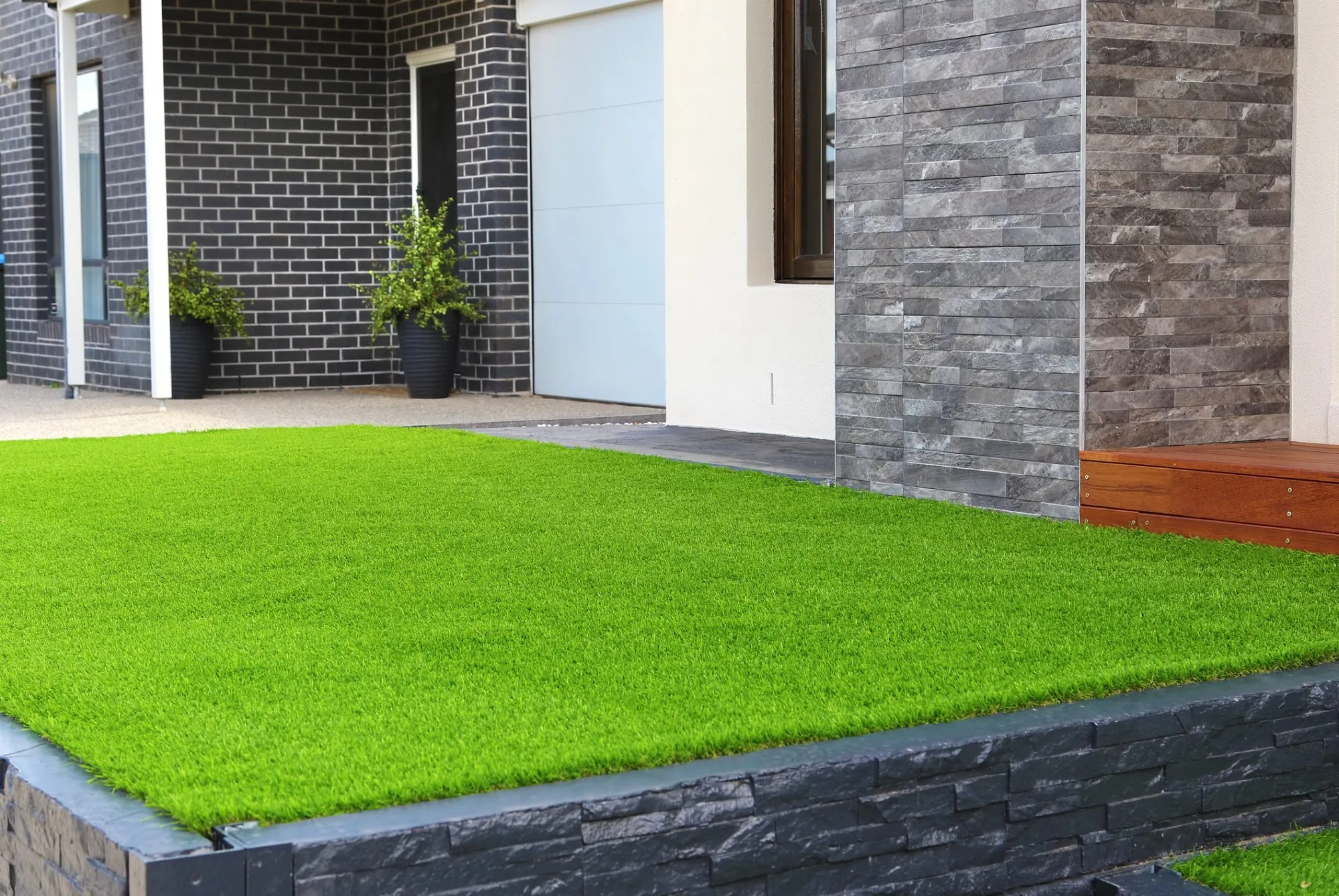 A pristine raised artificial grass lawn bordered by modern dark grey stone cladding at a residential entrance.